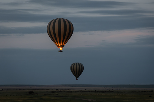 two (2) hot air balloons in the air with flame visible from one balloon