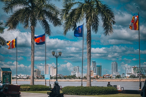 Phnom Penh, Cambodia - November 11, 2022:\nView from the old part of the city to the new modern part of Cambodia's capital, Phnom Penh. Photo taken from Sisowath, Phnom Penh Riverside and include Cambodian flags.