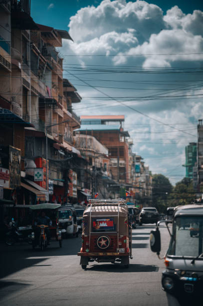 Phnom Penh, Cambodia - April 09, 2025: Tuk-tuk driving along the avenue and a view of Moonlight Pavilion