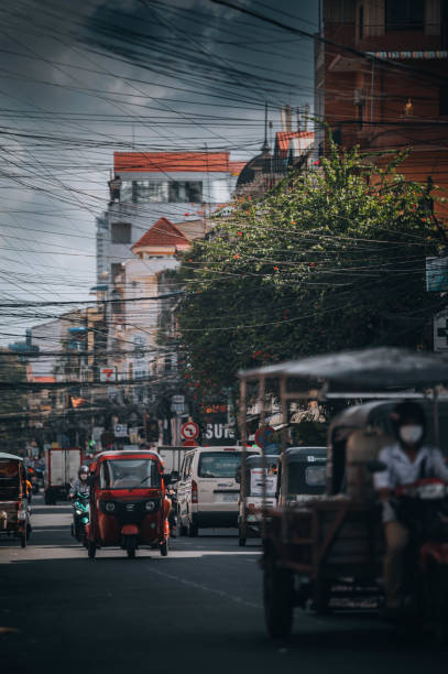 Phnom Penh, Cambodia -November 11, 2022: A busy scene with people riding through the city on a three wheels vehicle and a motorcycles in Cambodia's capital, Phnom Penh.