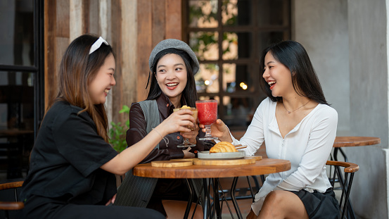 A group of trendy, happy Asian girls are drinking and enjoying talking in a cafe in the city on the weekend together. City life, friendship, lifestyle