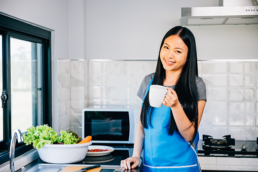 In a cozy kitchen a smiling woman stands holding a cup of coffee portraying relaxation and enjoyment. Illustrating a cheerful morning routine in a comfortable home environment.