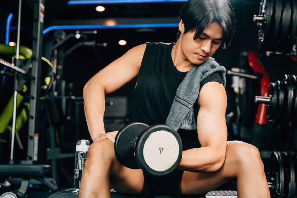 istock handsome young Asian man sitting on an exercise bench holding a heavy dumbbell 1863813581