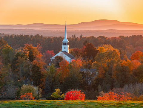 landscape of church tower in autumn mountain forest during sunset