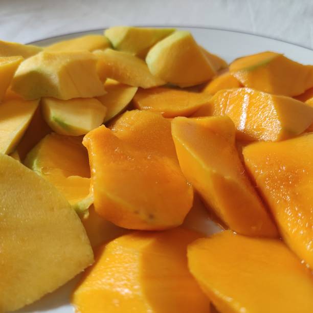 istock Fresh yellow mango slices on a plate on a white table background 1863830182