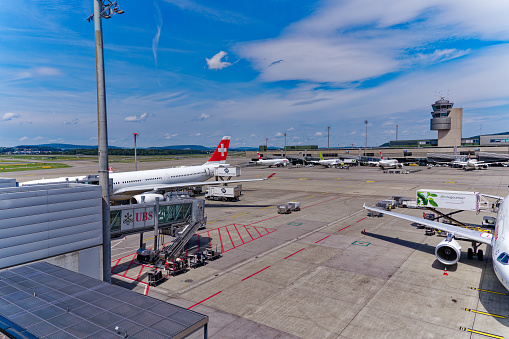 Parked airplanes with air traffic control tower in the background at Zürich Kloten Airport on a sunny summer day. Photo taken July 23rd, 2023, Zurich, Switzerland.