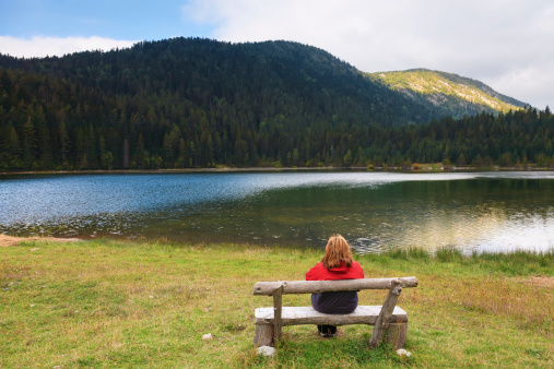 Lonely woman sits on a bench and watching the mountain Lake