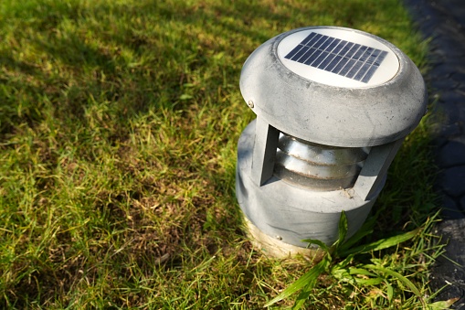 Close up an automatic solar cell lantern for garden ,setting on the green grass in sunny day,sunshining to the solar lantern lights in afternoon time.Trees shadow on green grass background.