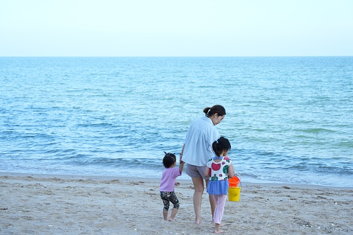 Afternoon beach front with a family tourist ,mother hand holding her childs  walking along the beach,one dhild hand holding bucket for sand playing ,beautiful beach front at Cha-am beach , Phetchaburi province,Thailand.