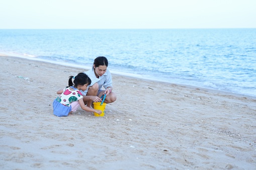 Seaview with close up mother and her daugther enjoy  playing  sand on the beach ,child hold small bucket put something into bucket.Beautiful beach front at Cha-am beach , Phetchaburi province,Thailand.