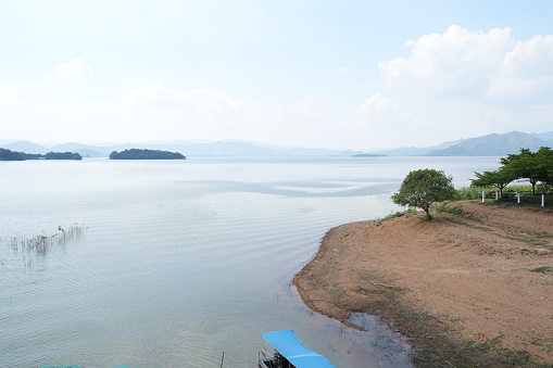 View of Kaeng Krachan Dam ,sunshine on clouds sky in sunny day ,lake and Mountain background. transparent water with small waves on the shore of lake ,Kaeng Krachan National Park in Thailand.
