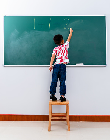 A boy writing 1+1=2 on chalkboard