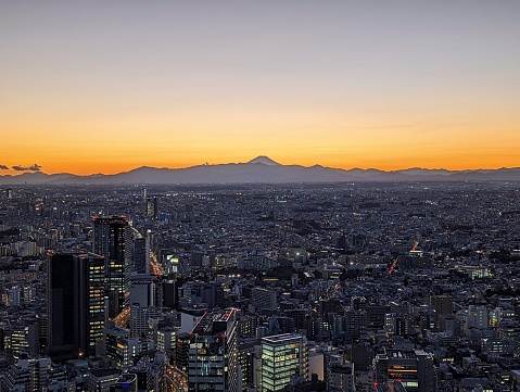 Panoramic view of the city scape of Tokyo with a bright orange Mt. Fuji in the background during sunset in Japan