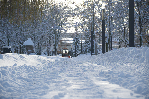 Snow-covered street and snow removal vehicle parked on the street, showing that it is actively clearing the path for traffic, street itself is bordered by high banks of drifted snow