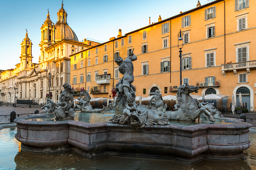 rome, Piazza Navona,  the rays of the rising sun reflecting from the church of Sant'Agnese in Agone, the Fountain of the Four Rivers with its obelisk in the foreground.