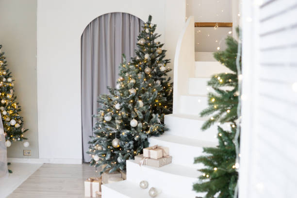 A large Christmas tree in the living room, decorated with garlands and light balloons. Bright Christmas interior with a white staircase. stock photo