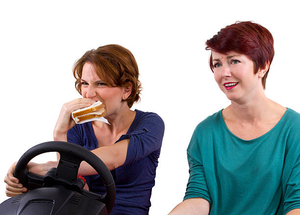 istock Female Driver Eating a Sandwich and Driving with a Passenger 186410961
