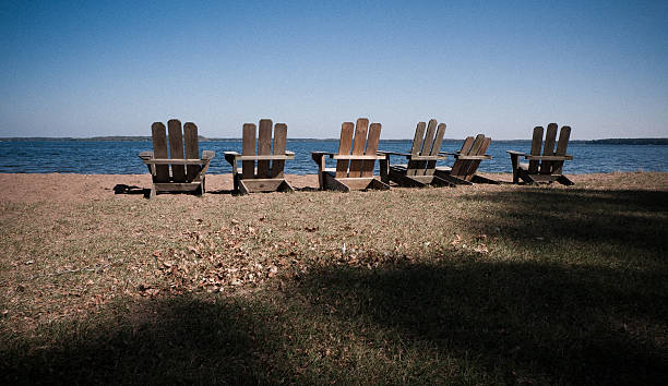 Six wooden Adirondack chairs face lake stock photo