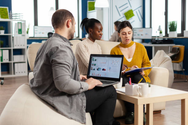 istock Businessman holding laptop with financial ghraphics while diverse employees talking 1864133647
