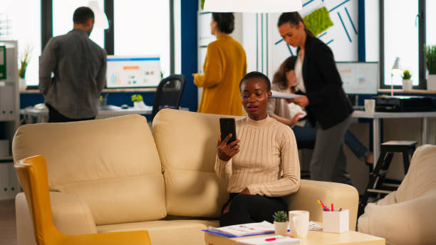 Tired black woman talking with colleague using video call holding smartphone