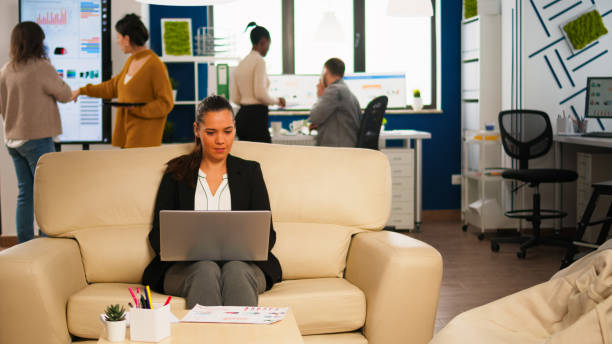 istock Manager woman holding laptop, looking on internet while sitting on couch smiling 1864154136