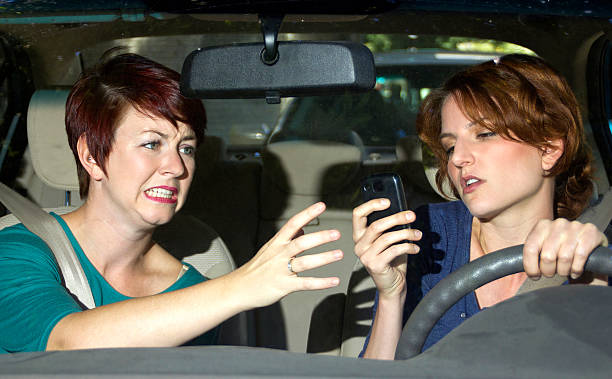 istock Woman driving and looking at a phone while other argues 186416575