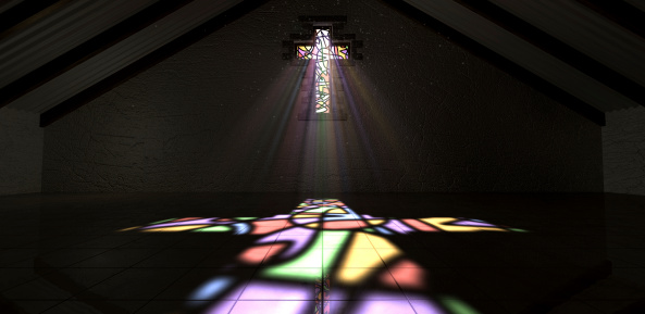 An interior building with a colorful stained glass window in the shape of a crucifix with a spotlight rays penetrating through it reflecting the image on the floor