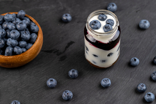 ripe blueberry berries and yogurt with blueberry and blueberry flavor , large blueberry berries and yogurt in a glass jar on a black slate board