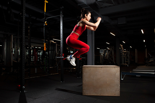 athletic woman in red sportswear training in black gym, slim girl jumping in fitness hall, attractive woman on gym endurance training