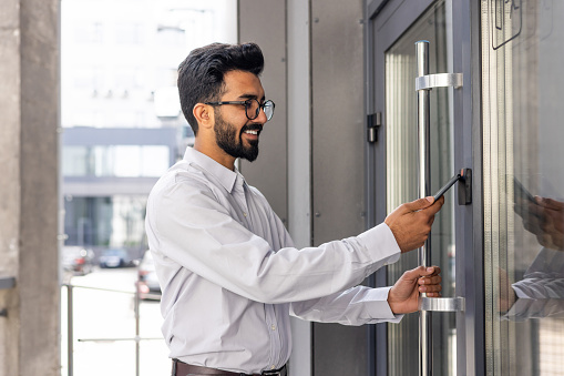 Young businessman using phone to open office door of building, man happy using wireless access, businessman going to work happy smiling.