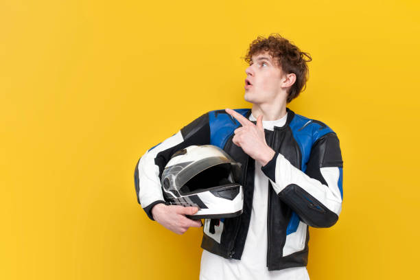 istock young guy motorcyclist in leather jacket holds helmet and points to the copy space on yellow isolated background 1864223017