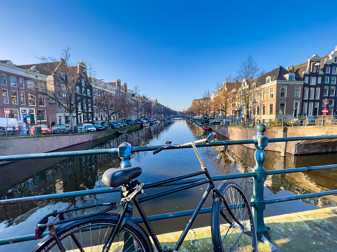 Bicycle leaning against the canal railings in Amsterdam, sunny and cold winter day. Beautiful cityscape of Amsterdam. Typical Dutch canal surrounded by trees. Sun shining and creating long shadows.  Travel destination and transport background, copy space.