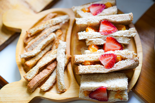 Side view of a homemade vegetarian sandwich stuffed with fried egg, fresh strawberries and crispy whole wheat breadsticks on a plate on a kitchen table.