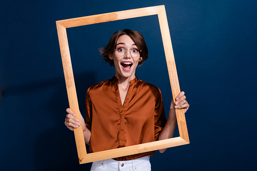 Photo portrait of lovely young lady hold wooden frame excited photo dressed stylish brown blouse isolated on dark blouse color background.