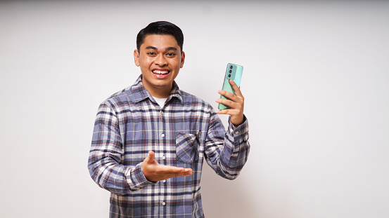 Young Asian man showing happy gesture while looking to his mobile phone on white background. studio shot
