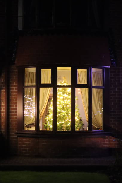 istock Christmas tree at night through a house window, covered in lights and decorations 1864299084