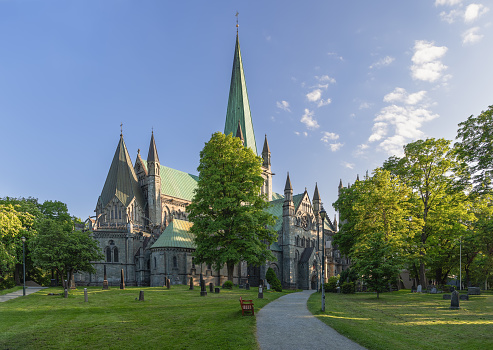 Park path meanders through a well-maintained cemetery, leading towards the majestic Nidaros Cathedral in Trondheim, Norway