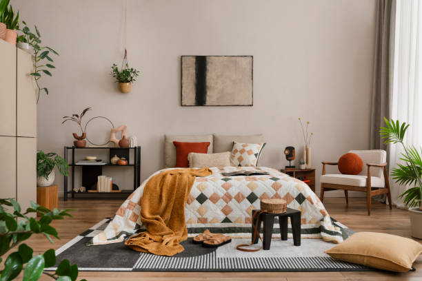 istock Warm and cozy bedroom interior with mock up poster frame, beige and orange bedding, patterned rug, black rack, plants, red armchair, plaid, curtain and personal accessories. Home decor. Template. 1864331829
