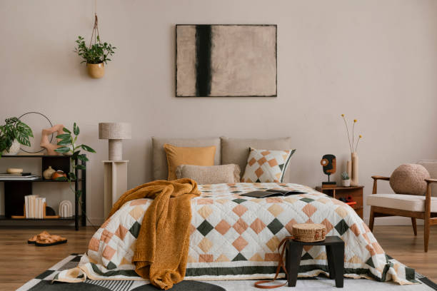 istock Warm and cozy bedroom interior with mock up poster frame, beige and orange bedding, patterned rug, black rack, plants, red armchair, plaid, curtain and personal accessories. Home decor. Template. 1864332367