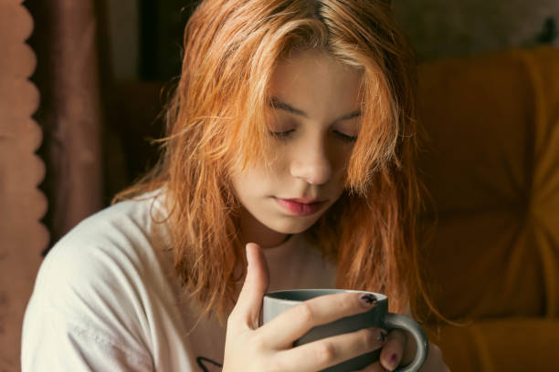 istock Charming Generation Z Red-Haired Teenager Enjoying Hot Cup by Window 1864345332