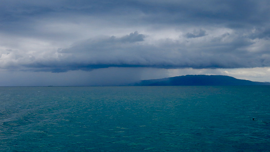 Thunderclouds and rain in the distance over the blue sea.