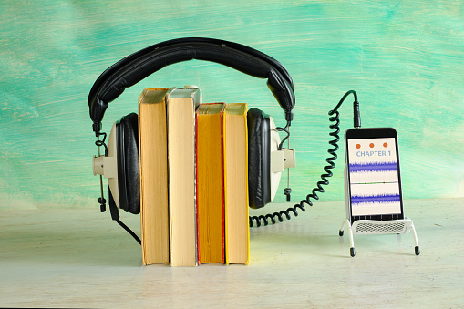 audio book concept with row of books,vintage headphones and smartphone displaying audio wavepatterns, green background, free copy space