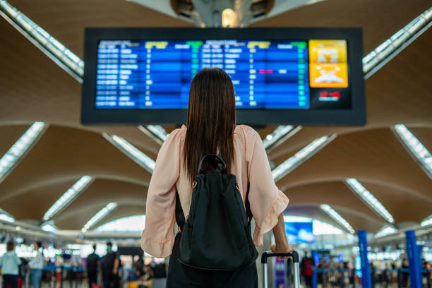 businesswoman standing in airport rear view of businesswoman standing in front of departure ariival board of international airport looking at the flight information board klia airport stock pictures, royalty-free photos & images