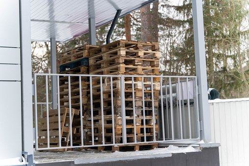 A neat stack of wooden pallets arranged at a store's unloading area, ready to be used for shipping goods. The rough texture of the wood contrasts with the smooth ground.
