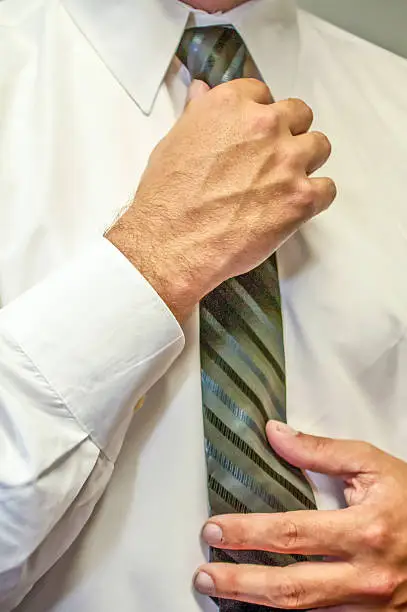 man fixing a tie with hands in white shirt