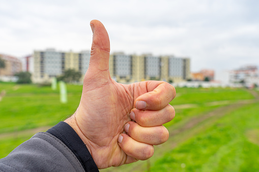white man's hand doing a cool thing against a background of forest and urbanized area with buildings in the background evoking the fact that the buildings are pleasant