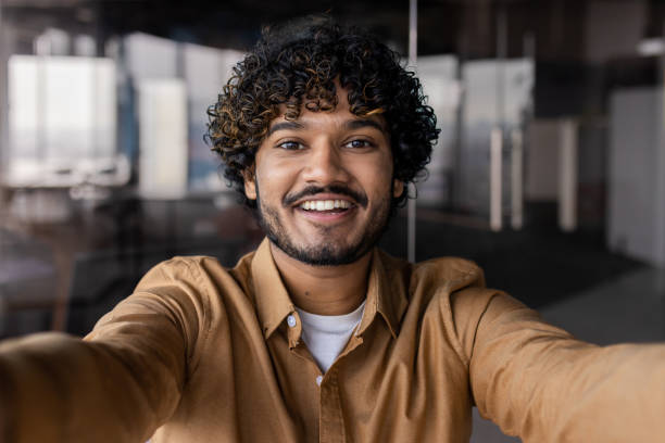 istock Video ringing, successful businessman looking at smartphone camera talking remotely with colleagues, Hispanic man smiling at work inside office, webcam view pov 1864418040