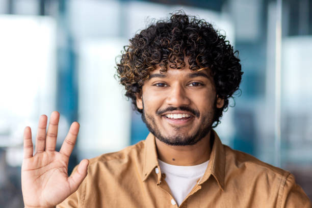 istock Young man smiling and looking at camera, waving hand greeting, businessman inside office building, talking with colleagues and friends partners 1864418588