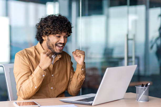 istock Successful businessman winner at workplace inside office, man received online message about successful results financial achievement, working with laptop, holding hands up triumph gesture 1864418589