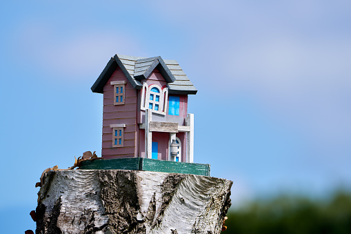 Colorful, weathered, little wooden house standing on a tree stump against blue sky